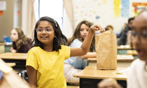 Child with brown bagged lunch at her desk in classroom